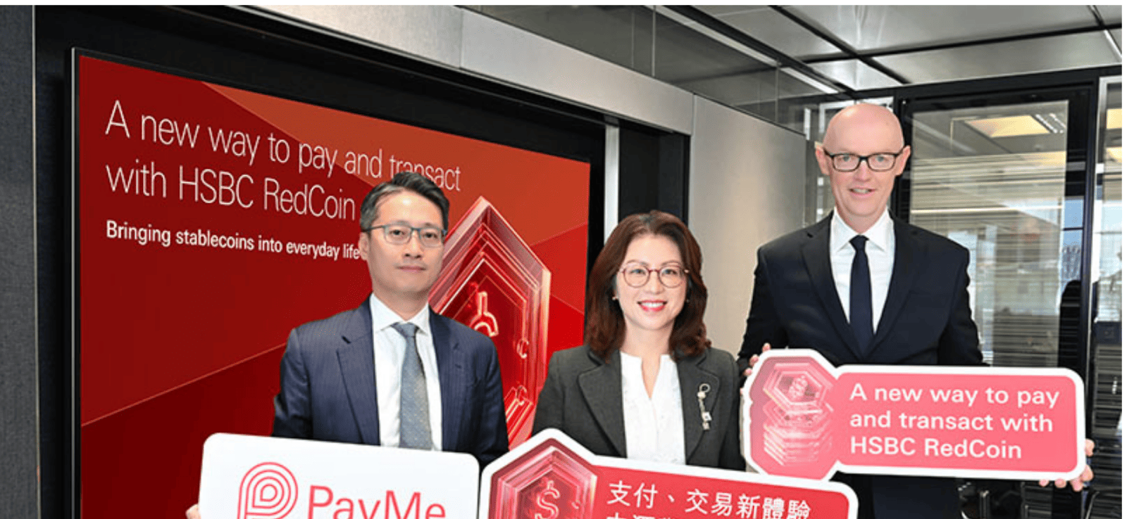 Drie HSBC-bestuurders bij de lancering van HSBC RedCoin, met borden van PayMe en RedCoin